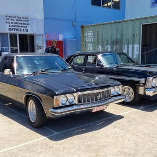 Two black Holden HZ Premier sedans parked outside the R & M Mechanical & Automatics shopfront